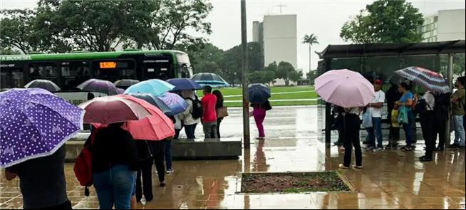 Sob chuva, pessoas aguardam ônibus em Brasília
